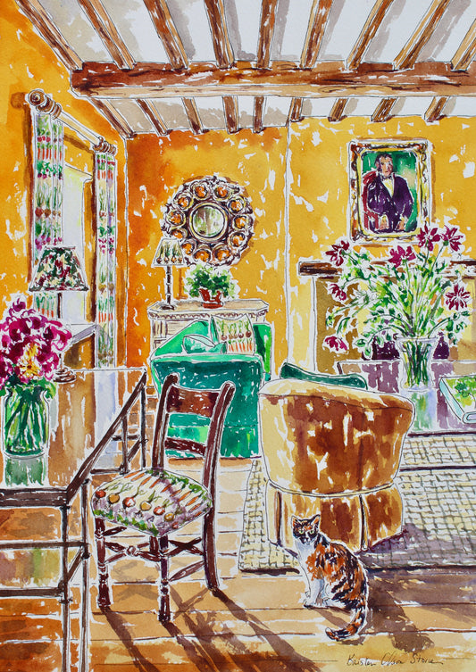 A designer interior of an English Gardener's Cottage with a calico cat.  Sunlight is pouring into the room casting beautiful shadows across the floor.  The walls are golden yellow and wood beams are on the ceiling. designer fabrics with carrots and radishes are on the chair and curtain fabric. 