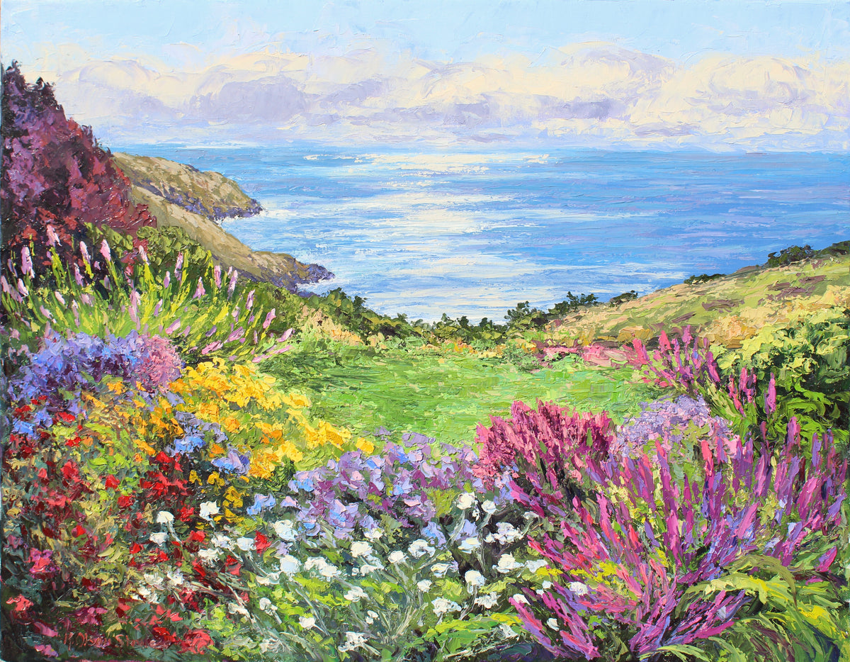 A green lawn and an abundance of flowers are blooming in a garden overlooking the ocean and sea cliffs.